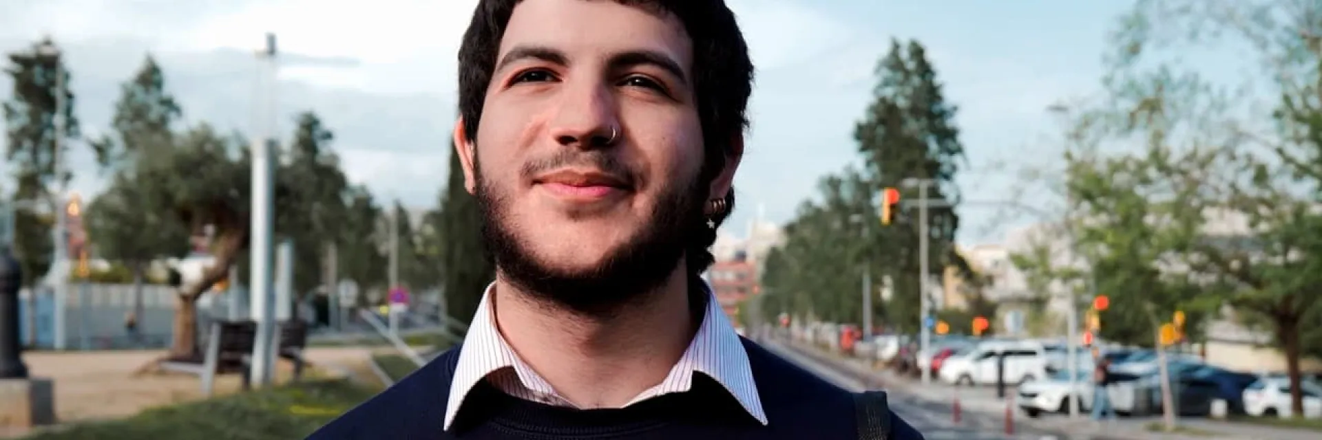 Hombre sonriendo en la calle mientras camina con camisa blanca y jersey azul