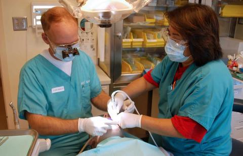 Dentista e higienista limpiando la boca de un paciente.