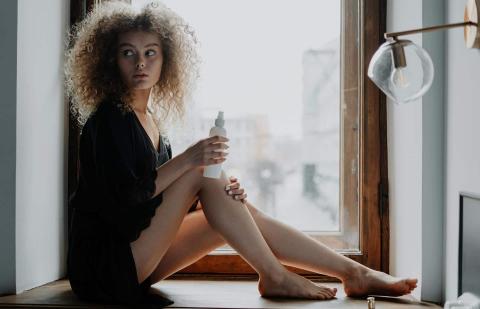 Una mujer joven aplica loción hidratante en las piernas porque tiene la piel seca.