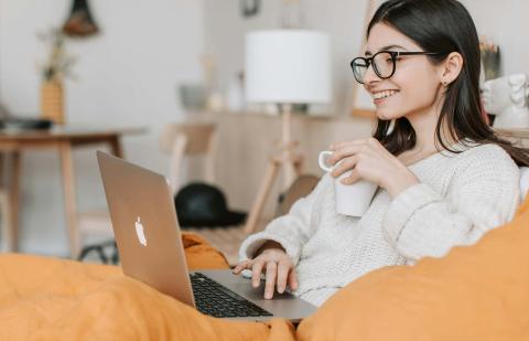 Chica en el sofá con un portátil, toma café y participa en clases online.