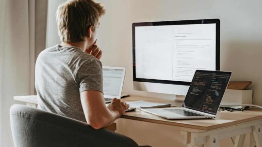 Un hombre con un monitor y dos portátiles, utiliza una API.