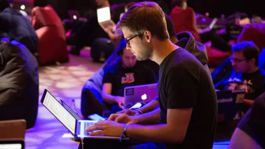 Estudiante con ordenador en una sala con más personas trabajando