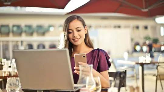 Una mujer navega por internet y usa el móvil en la terraza de un café.