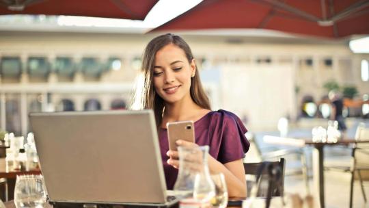 Una mujer navega por internet y usa el móvil en la terraza de un café.