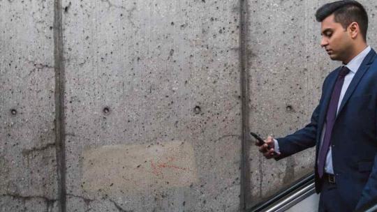 Hombre de negocios, que trabaja en relaciones públicas, bajando escaleras mecánicas y mirando su móvil.