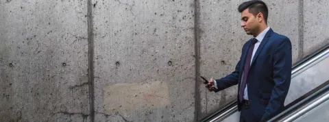 Hombre de negocios, que trabaja en relaciones públicas, bajando escaleras mecánicas y mirando su móvil.