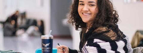 Estudiante joven sonriendo mientras escribe en su cuaderno