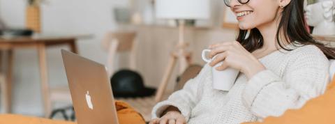 Chica en el sofá con un portátil, toma café y participa en clases online.