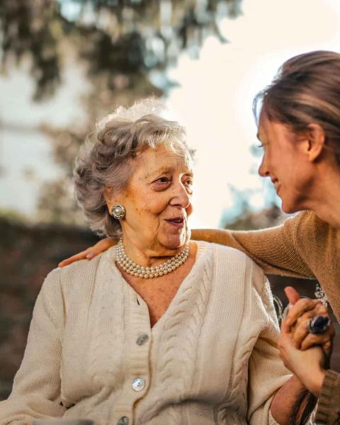 Una cuidadora de personas mayores sonríe, hablando con una paciente.