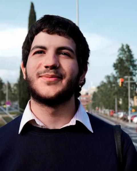 Hombre sonriendo en la calle mientras camina con camisa blanca y jersey azul